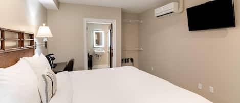 Une chambre d’hôtel avec un lit, un ventilateur de plafond, un téléviseur fixé au mur et une salle de bain visible à travers une porte ouverte.