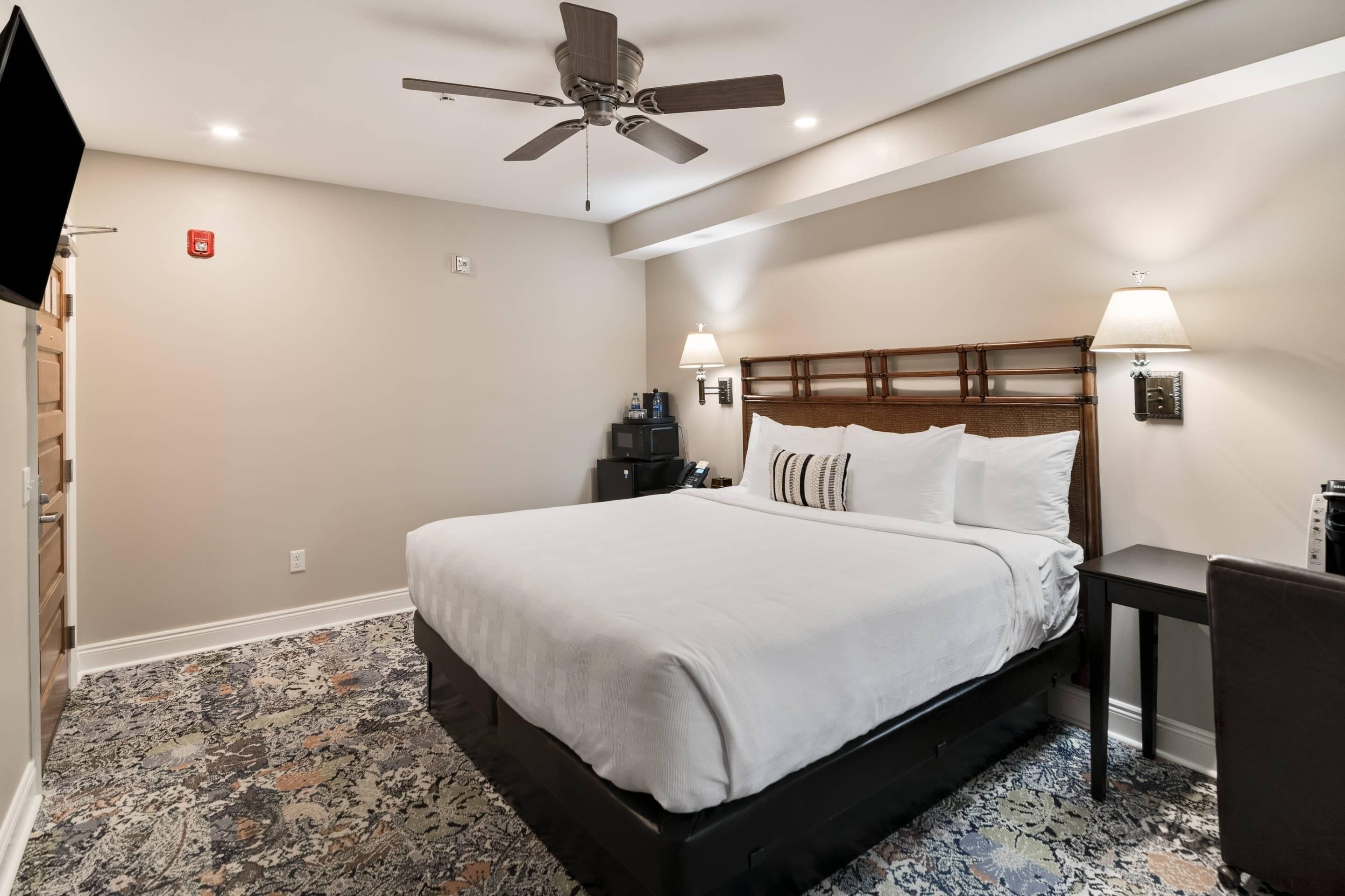 A hotel room with a bed, a ceiling fan, a TV, a desk, and a chair.