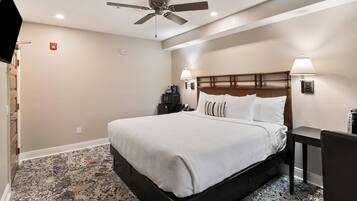 A hotel room with a bed, a ceiling fan, a TV, a desk, and a chair.