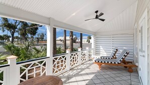 A covered outdoor area with a white ceiling, a ceiling fan, a wooden table, and two lounge chairs. - The Port Inn - Port St Joe, an Ascend Collection Hotel (Port St. Joe)