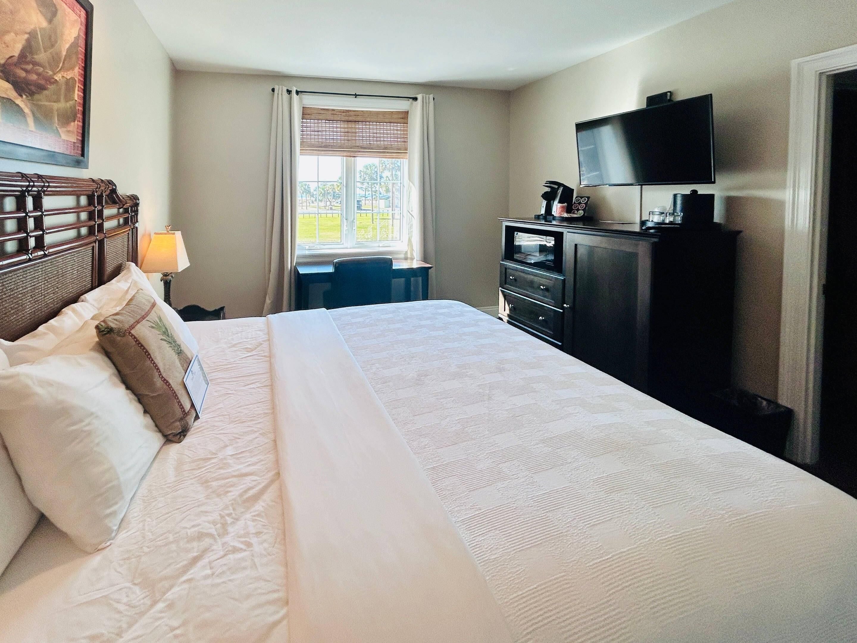 A hotel room with a large bed, a desk, a television, and a window with curtains.