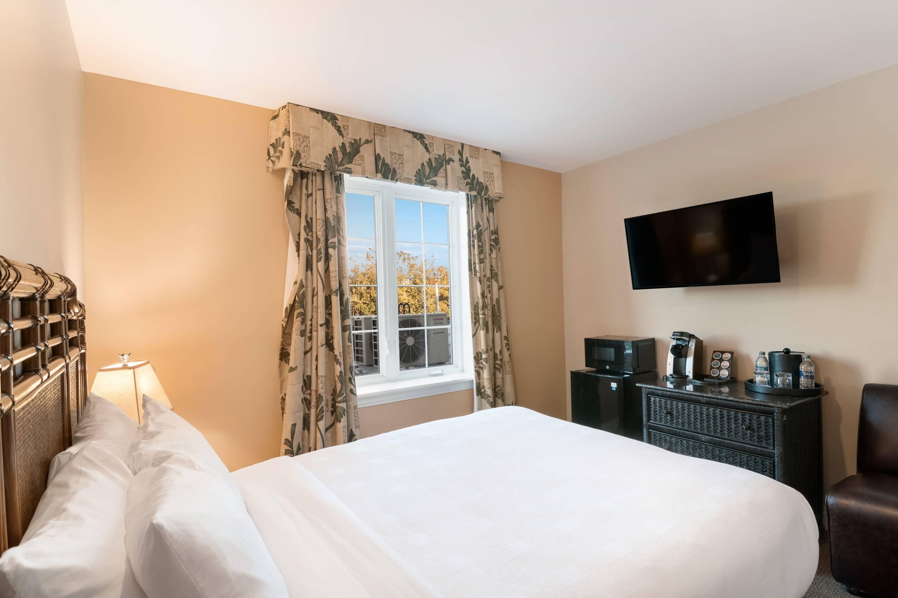 Une chambre d’hôtel avec un lit, une télévision, une commode et une fenêtre avec des rideaux.