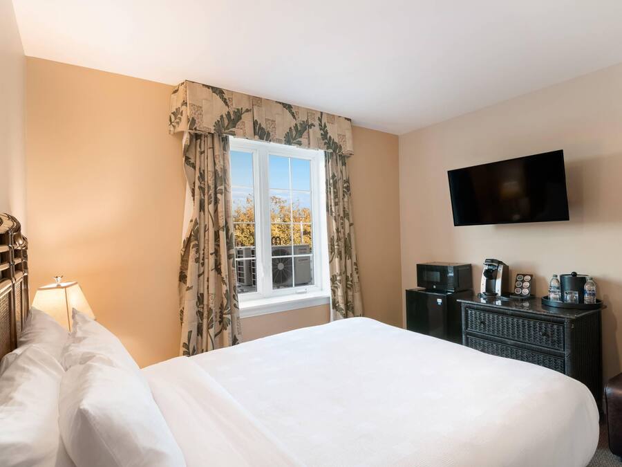 Ein Hotelzimmer mit Bett, Fernseher, Kommode und einem Fenster mit Vorhängen.