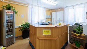A reception area with a wooden counter, a Coca-Cola refrigerator, and potted plants. - Pension Schwalbenweg (Schoenefeld)