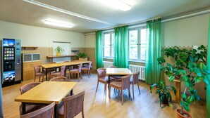 A dining area with wooden tables and chairs, a vending machine, and potted plants. - Pension Schwalbenweg (Schoenefeld)