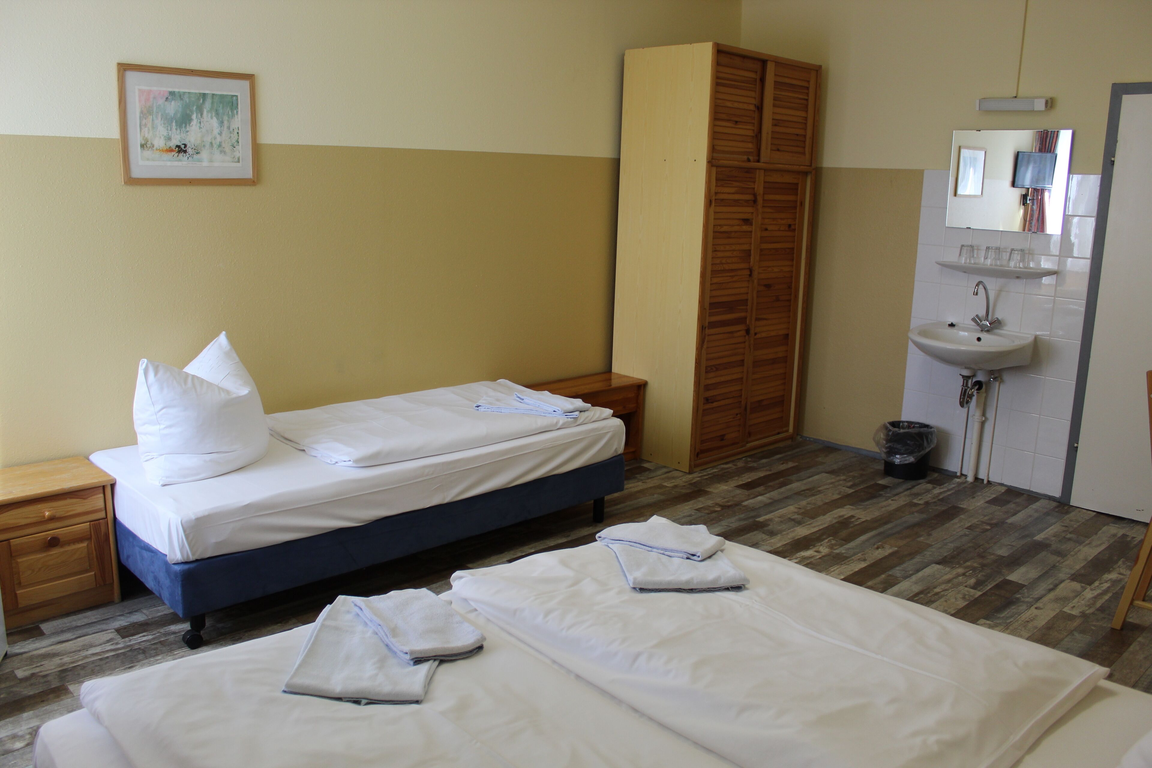 A hotel room with two beds, a wooden wardrobe, a sink, and a mirror.