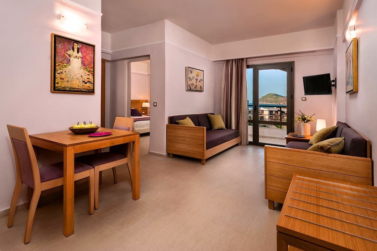 A modern hotel room with a dining area, a sofa, a bed, and a balcony with a view.