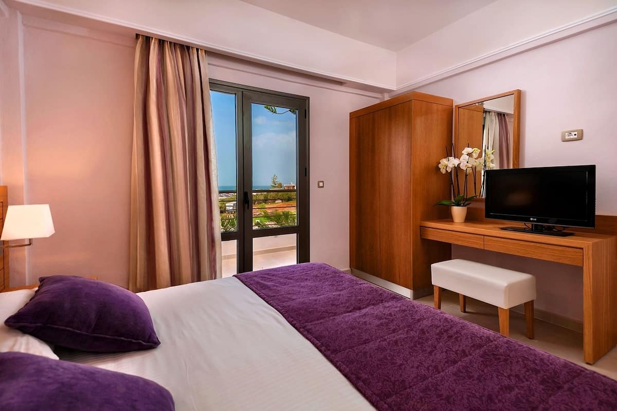 A hotel room with a bed, a desk, a television, and a view of the outdoors.