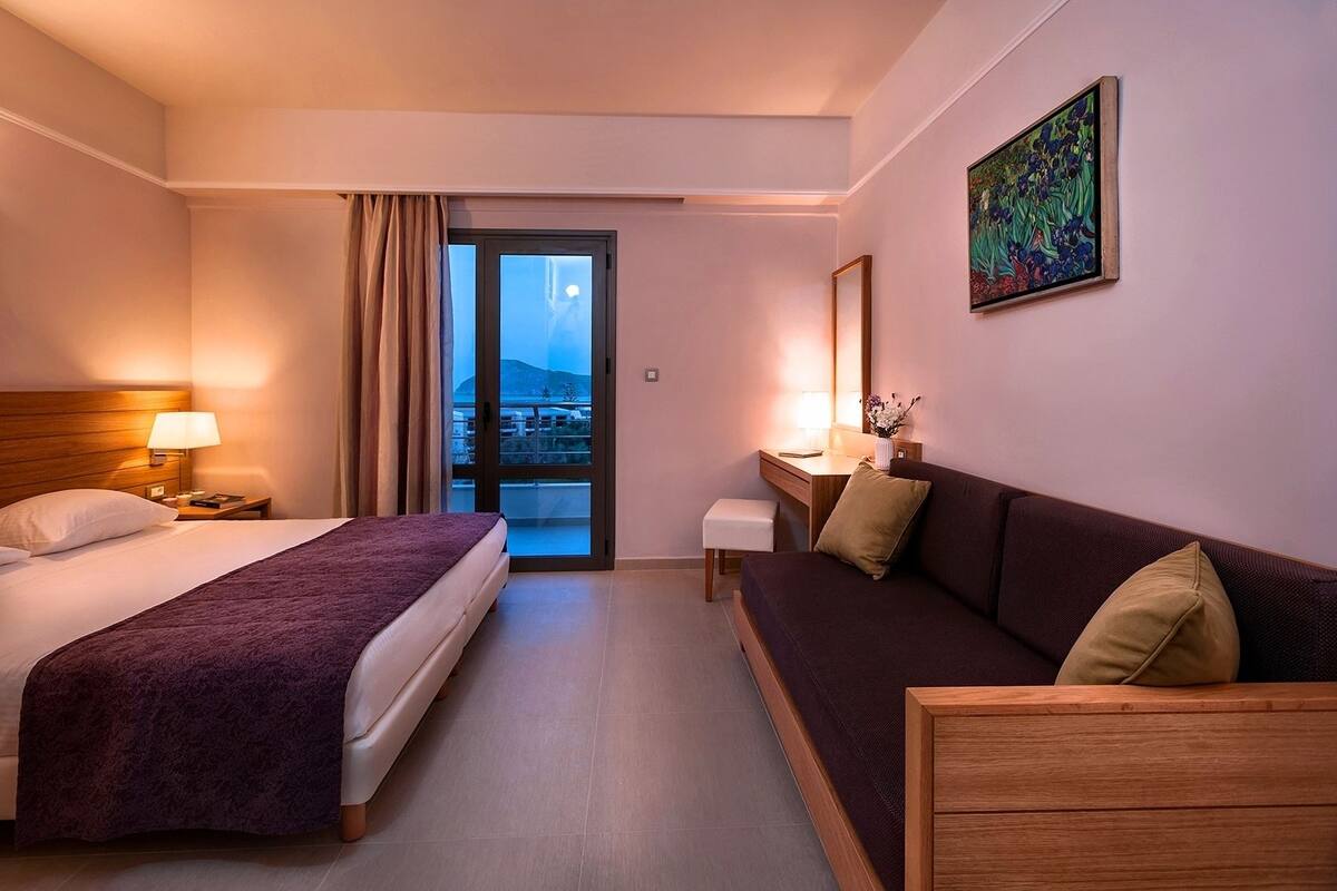 A hotel room with a bed, a sofa, a desk, and a balcony with a view.
