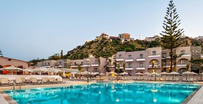 Un hotel con piscina, sillas de descanso y sombrillas.