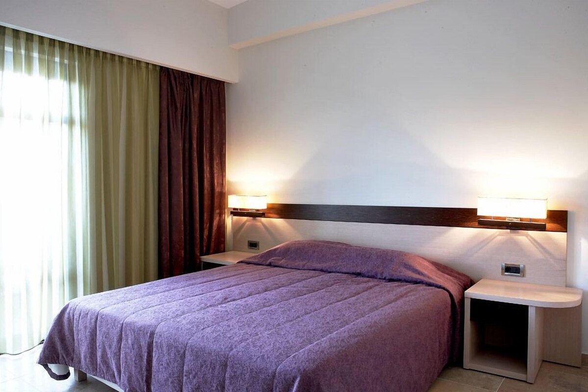 Una habitación de hotel con una cama, dos mesitas de noche y una mesilla.