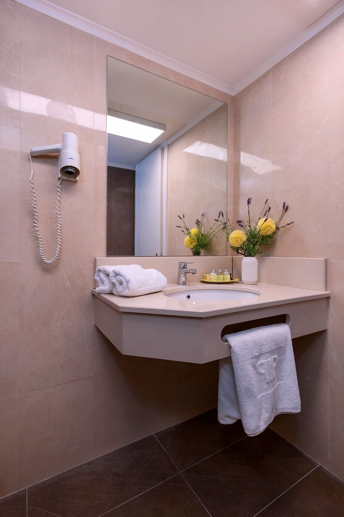 A modern bathroom with a large mirror, a sink, and a hairdryer mounted on the wall.