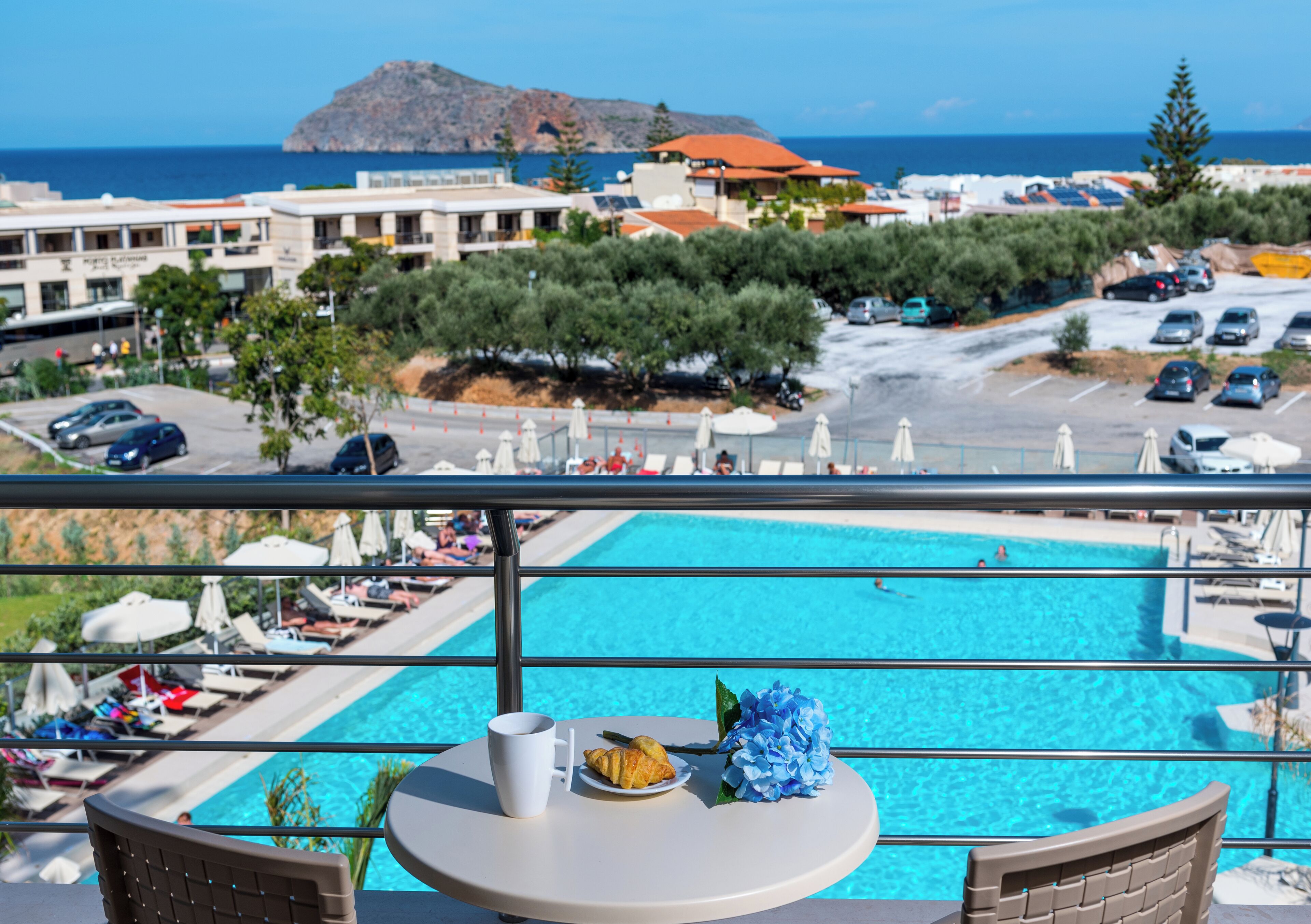 Un balcón con vista a una piscina, sillones de descanso y sombrillas.