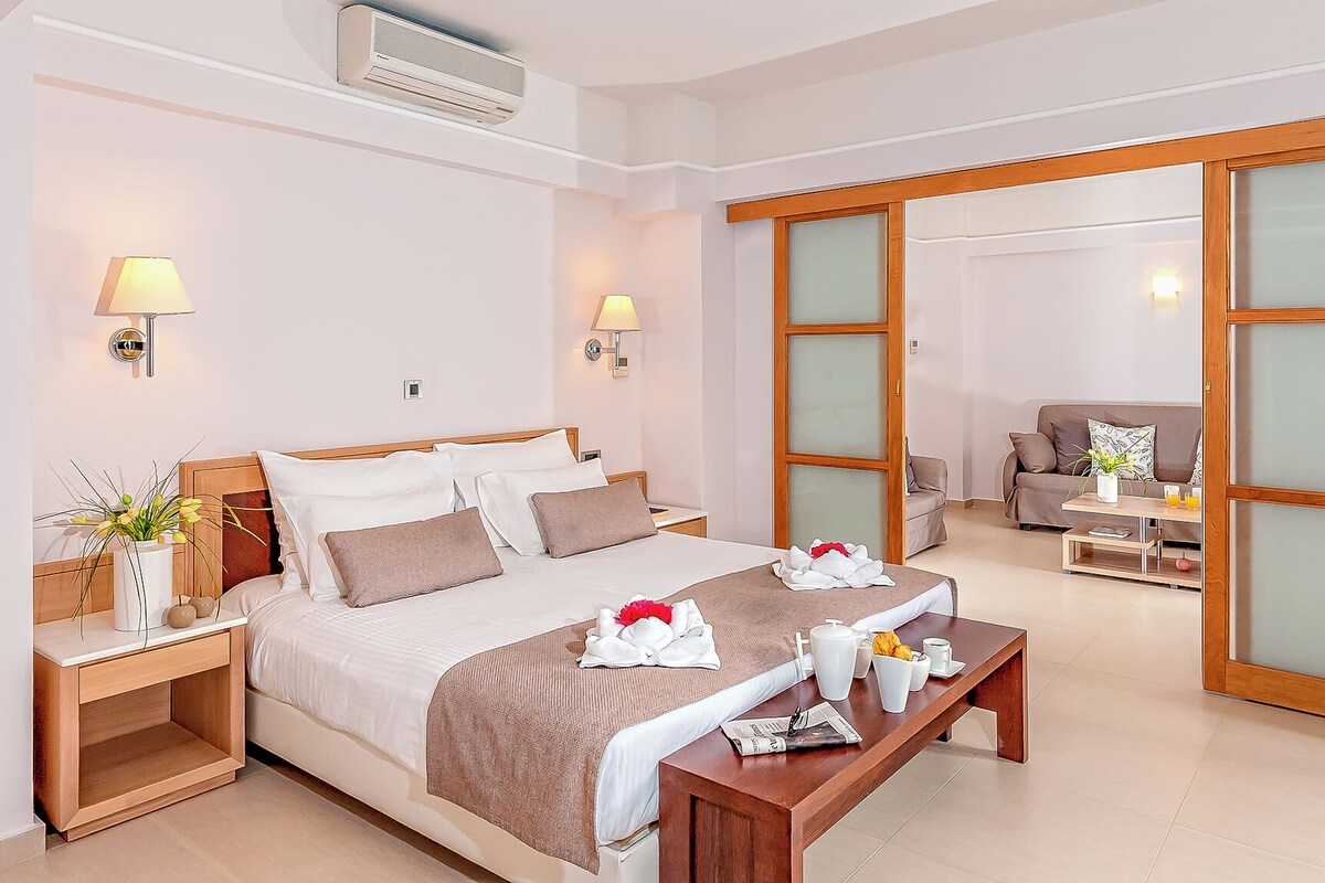 Una habitación de hotel con cama, mesitas de noche, una mesa de centro, un sofá y una puerta corrediza de vidrio.