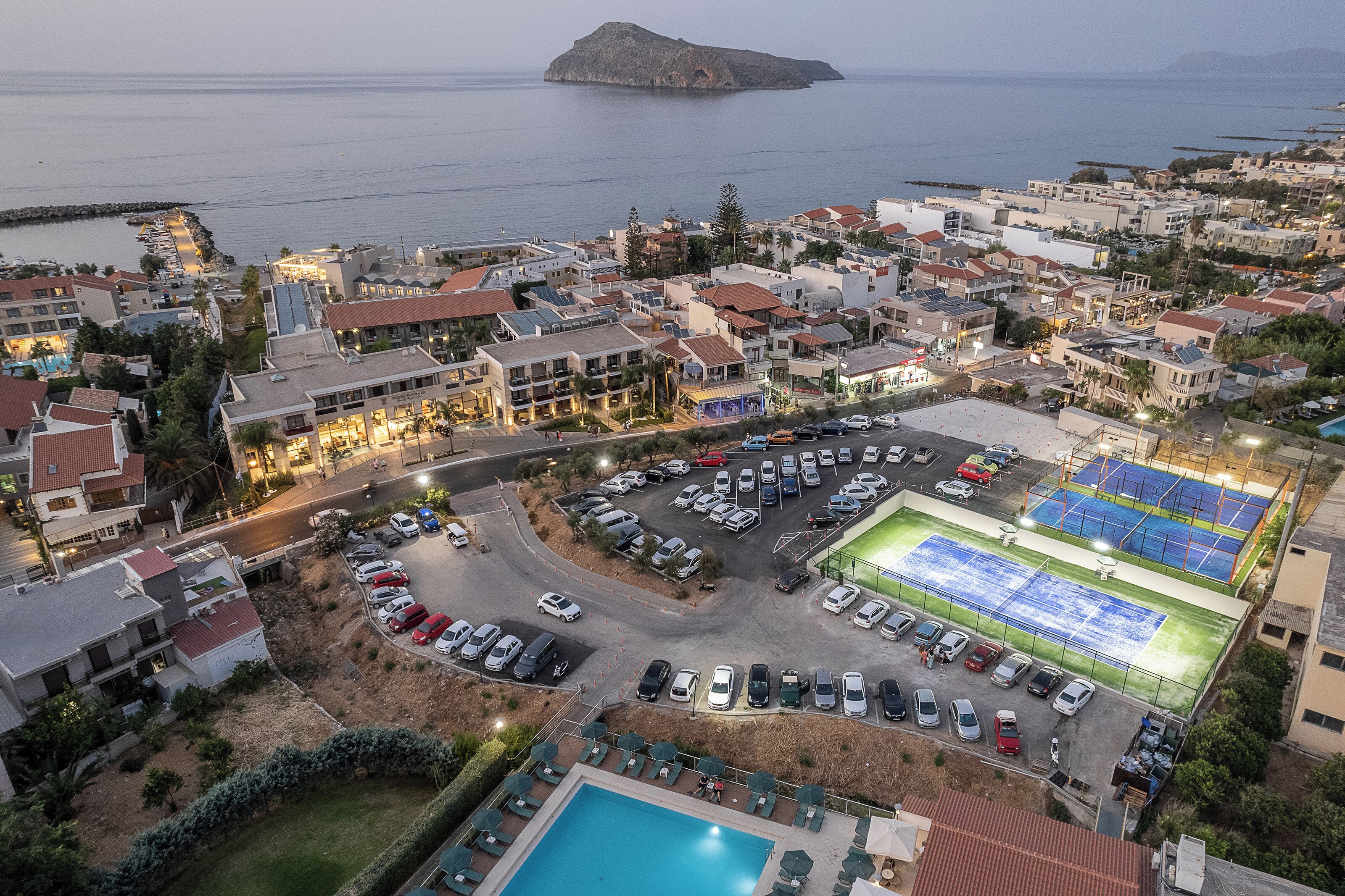 Vista aérea de un pueblo costero con un puerto deportivo, un estacionamiento amplio y una piscina.