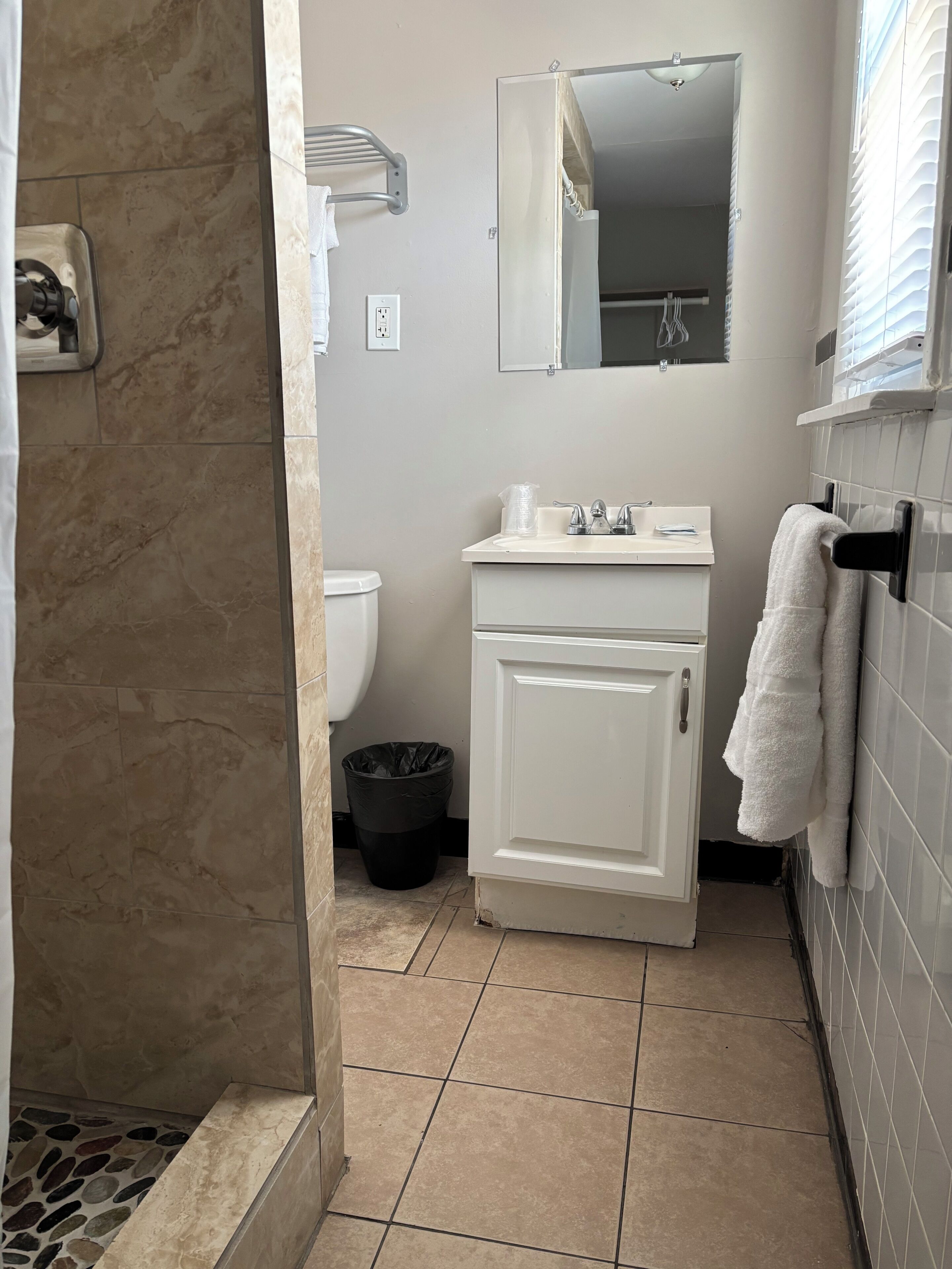 Baño con ducha, inodoro, lavamanos y espejo.