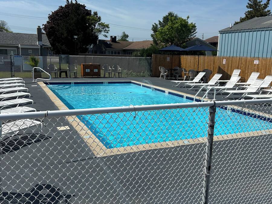 A swimming pool with a chain-link fence, lounge chairs, and a wooden deck.