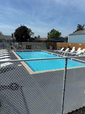 Piscina com cerca de arame, cadeiras de descanso e deck de madeira.