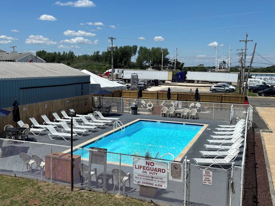 Une piscine entourée d’une clôture, avec des chaises longues et un panneau indiquant la présence d’un sauveteur.