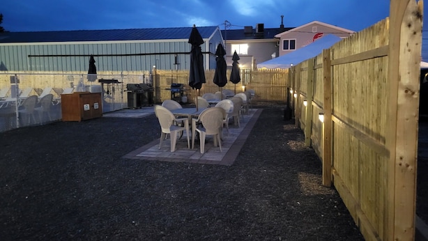 An outdoor patio with tables and chairs, a grill, and a wooden fence with lights.