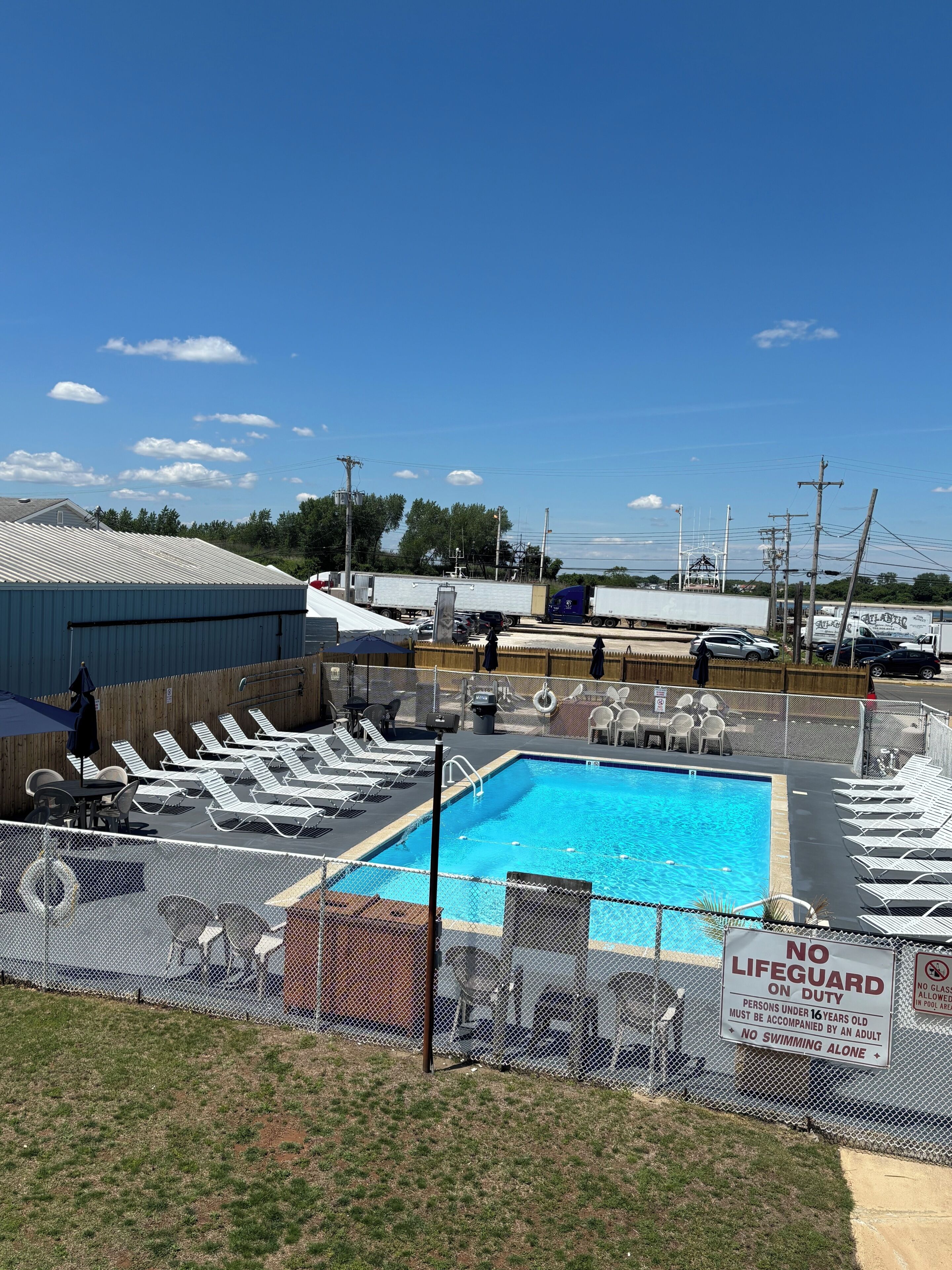 A swimming pool with lounge chairs, a fenced area, and a sign indicating no lifeguard on duty.