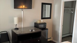 A hotel room with a bed, a desk with a lamp, a microwave, a mirror, and a wardrobe.