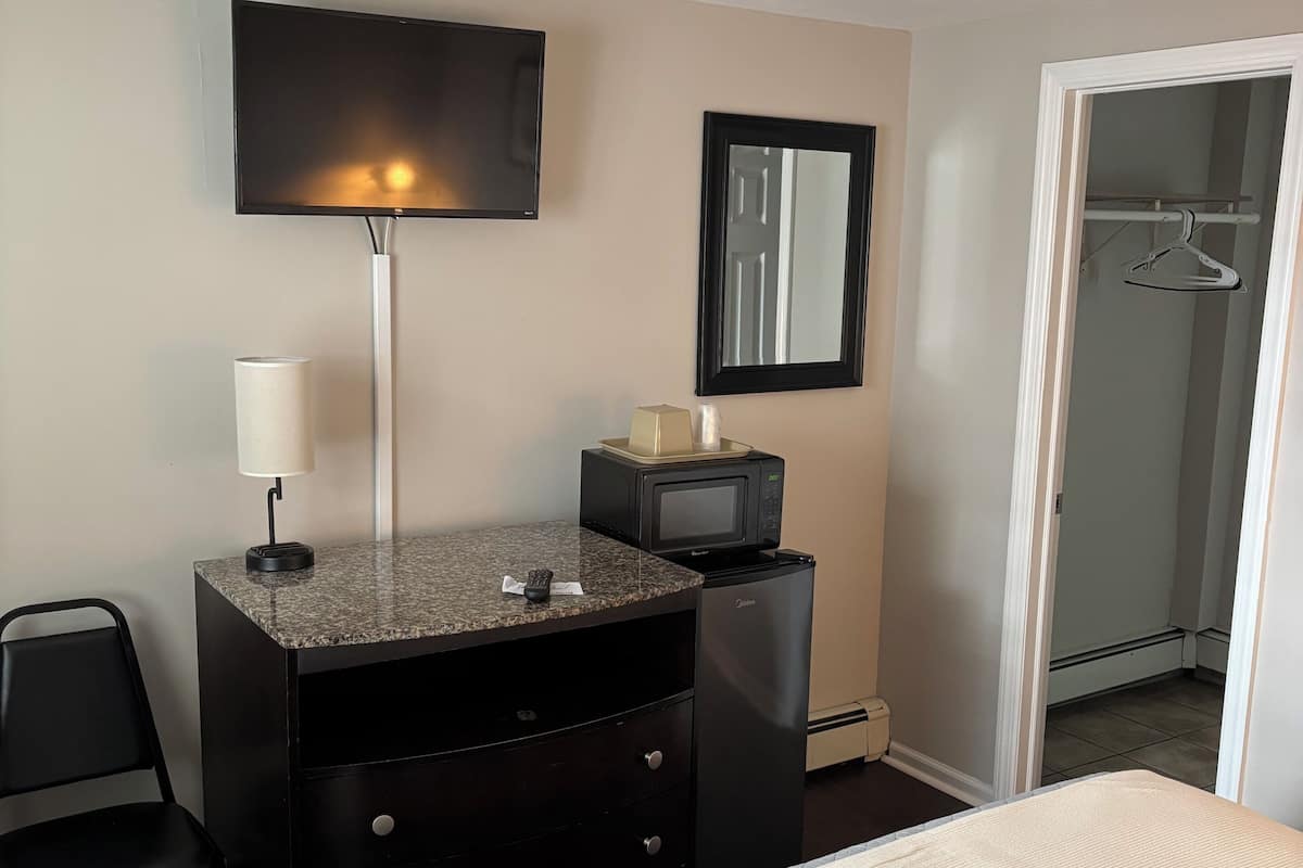 A hotel room with a bed, a desk with a lamp, a microwave, a mirror, and a wardrobe.