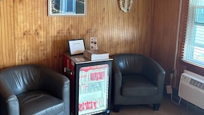 A room with wooden walls, two leather chairs, a refrigerator with beverages, and a ceiling fan.