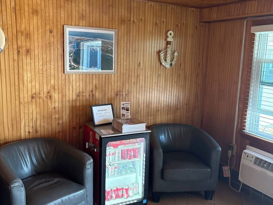 A room with wooden walls, two leather chairs, a refrigerator with beverages, and a ceiling fan.