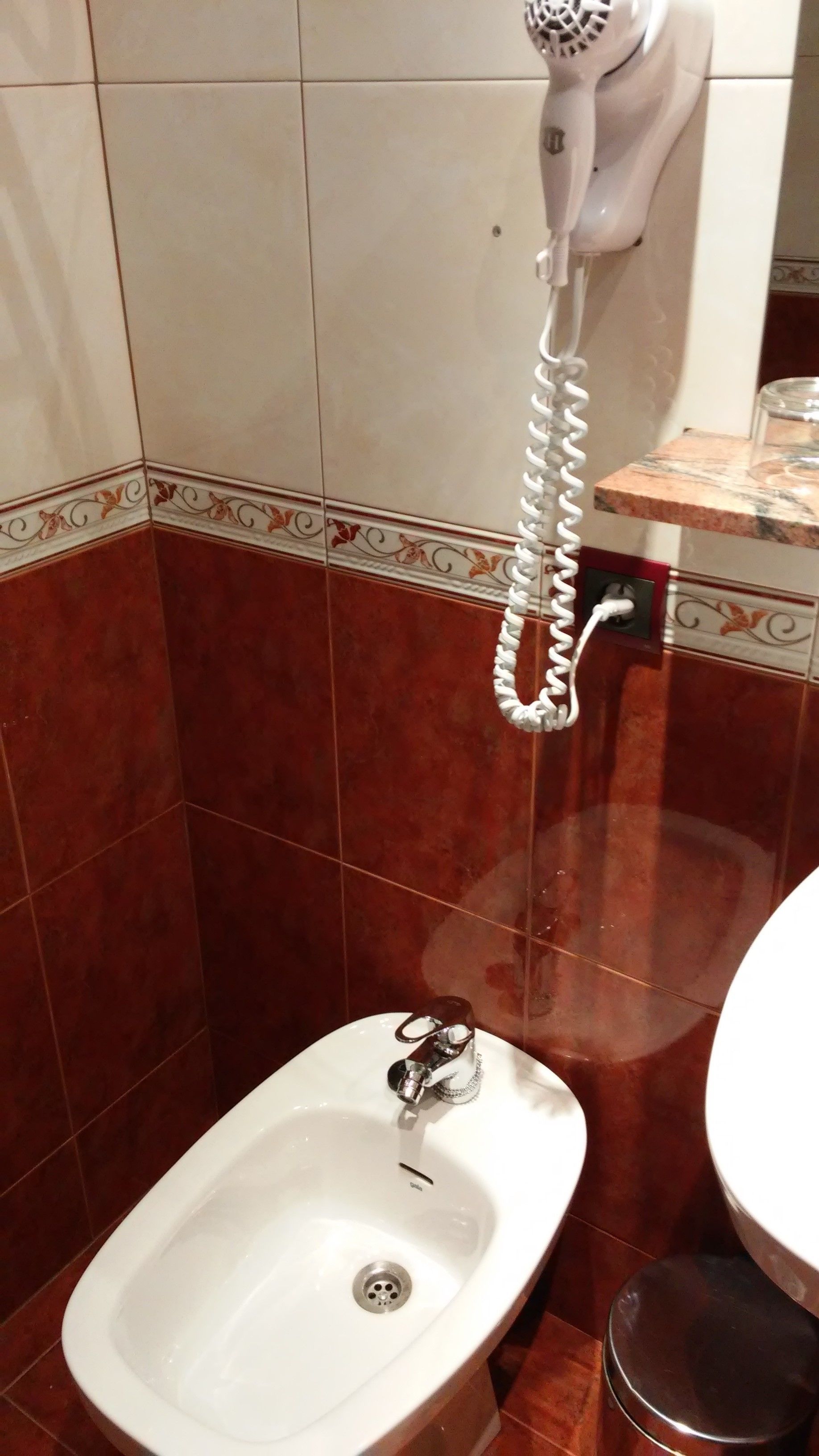 A bathroom with a bidet, a white sink, and a hairdryer mounted on the wall.