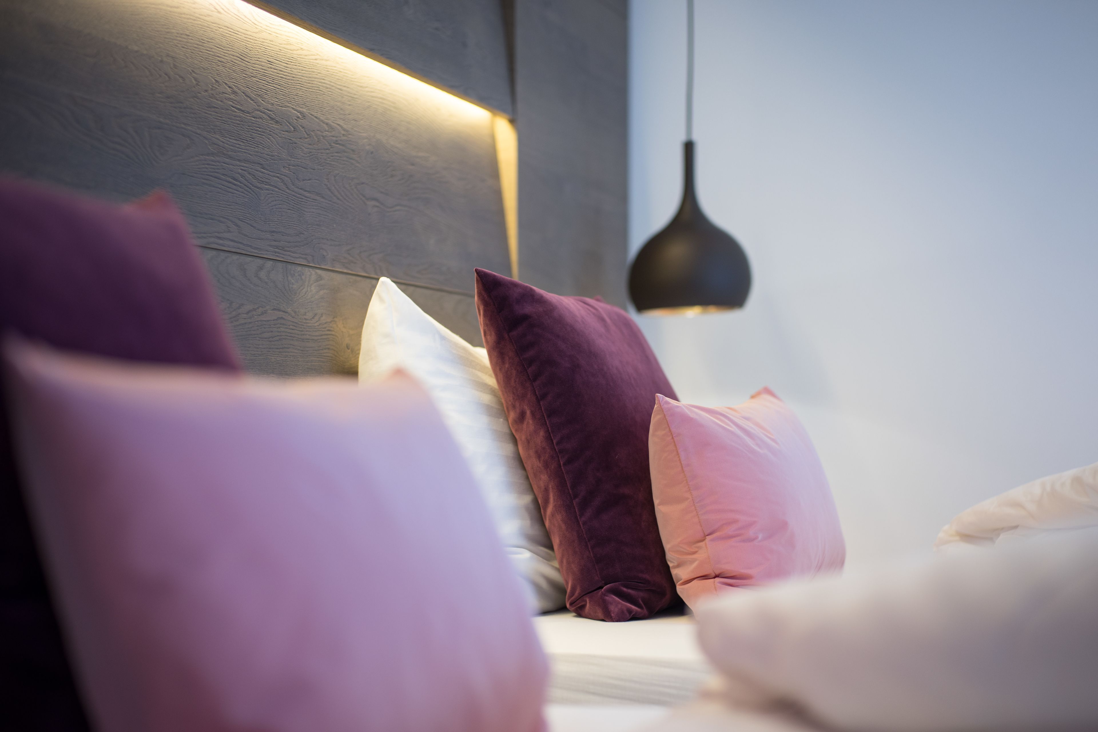 A bedroom with a wooden headboard, multiple pillows, and a pendant light.