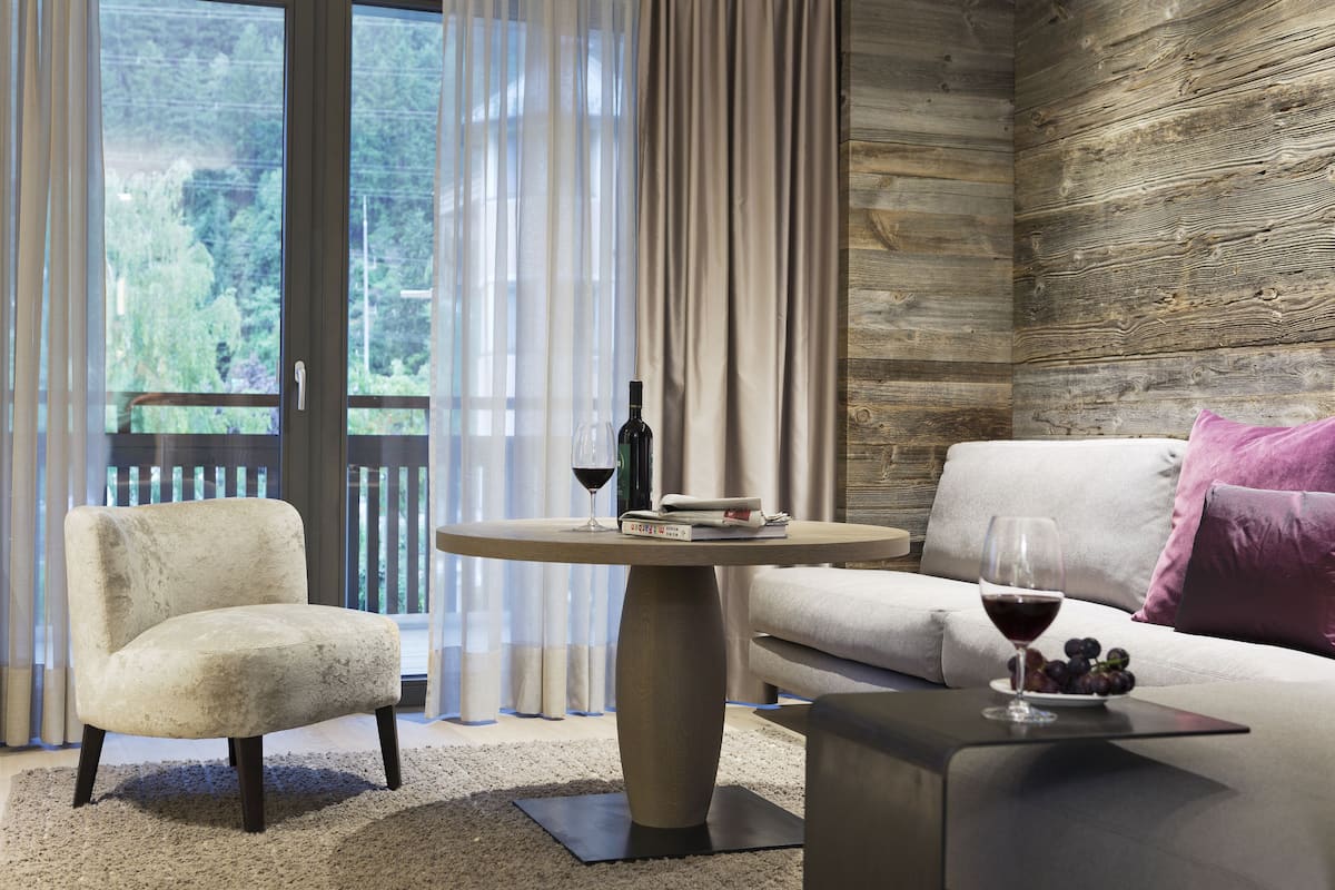 Un salon moderne avec un canapé, un fauteuil et une table basse ronde. On peut voir un verre de vin et une bouteille sur la table.