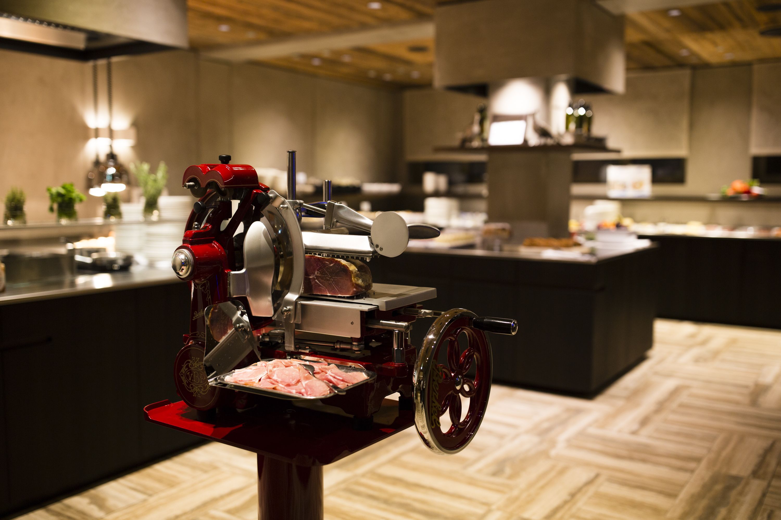 A kitchen with a meat slicer, wooden flooring, and modern appliances.