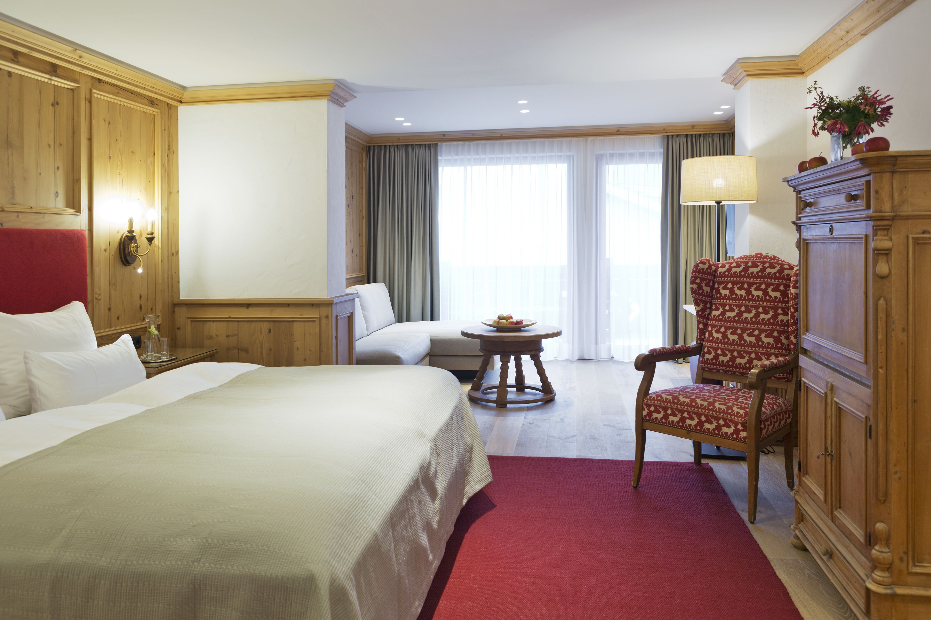 A hotel room with a large bed, a sofa, a chair, a small table with fruit, and a lamp.