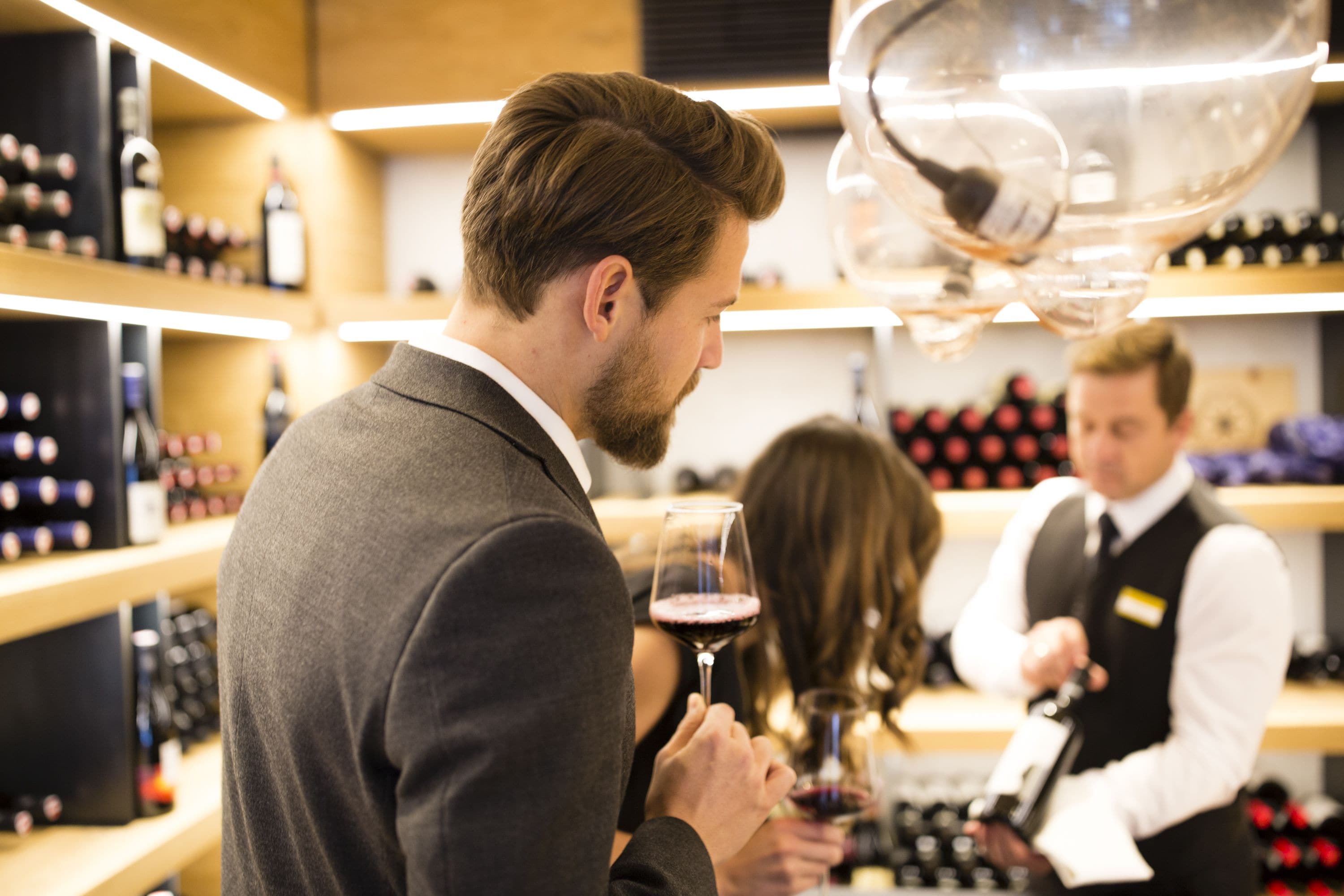 Un hombre sostiene una copa de vino en una tienda de vinos, con estantes llenos de botellas al fondo.