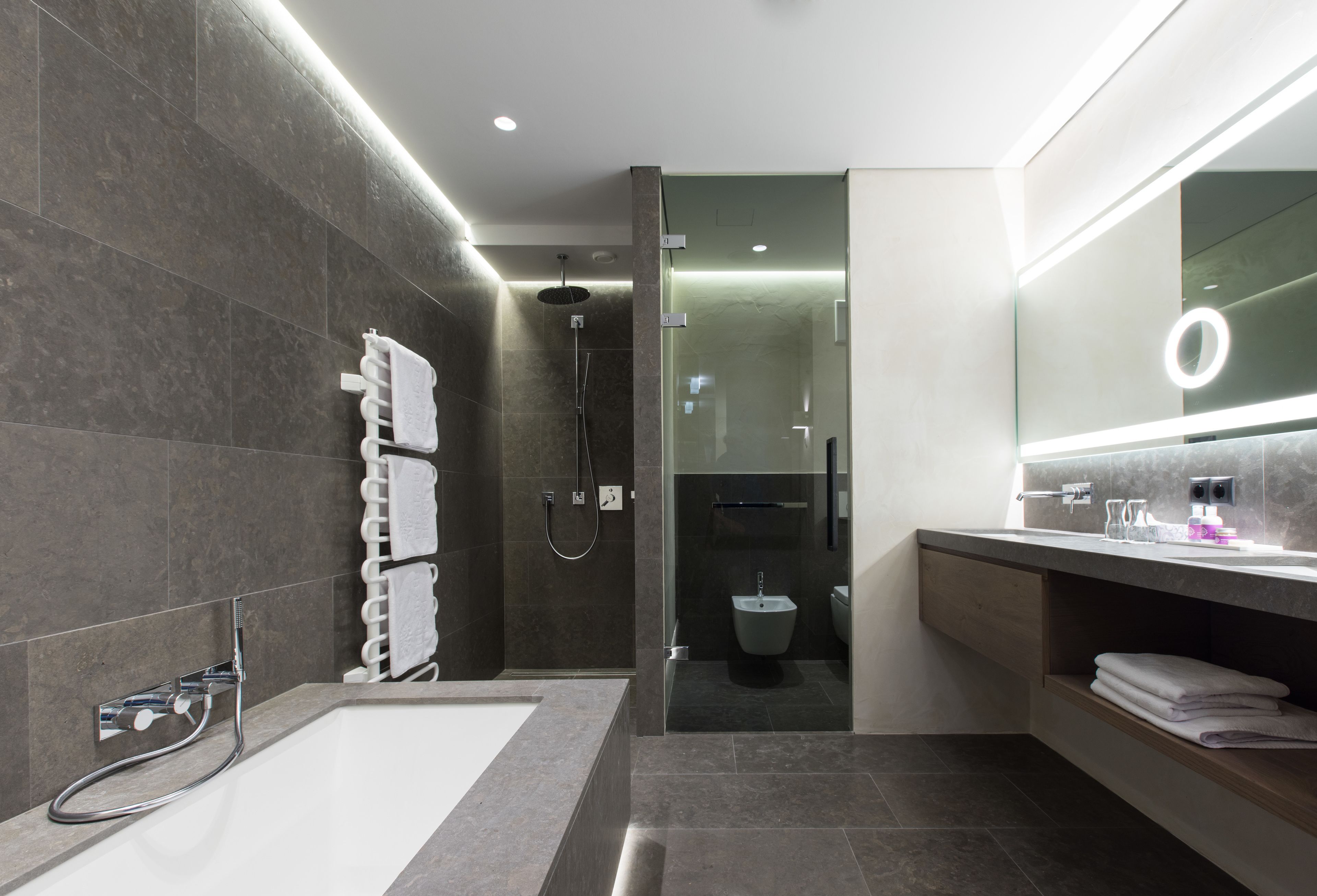 A modern bathroom with a bathtub, a glass-enclosed shower, a vanity with a mirror, and a towel rack.