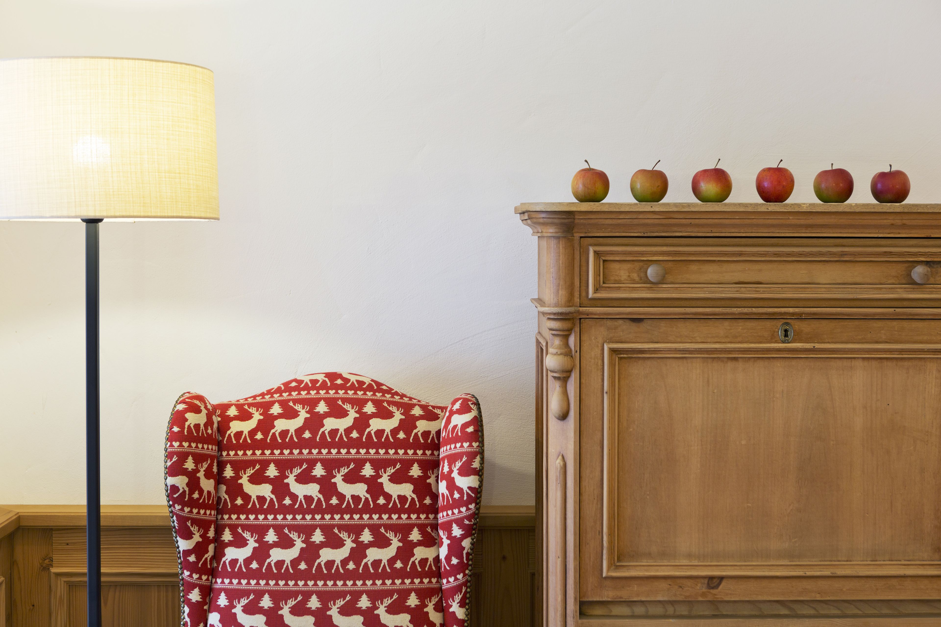 Una habitación con una lámpara, una silla con estampado de reno y un aparador de madera con manzanas encima.