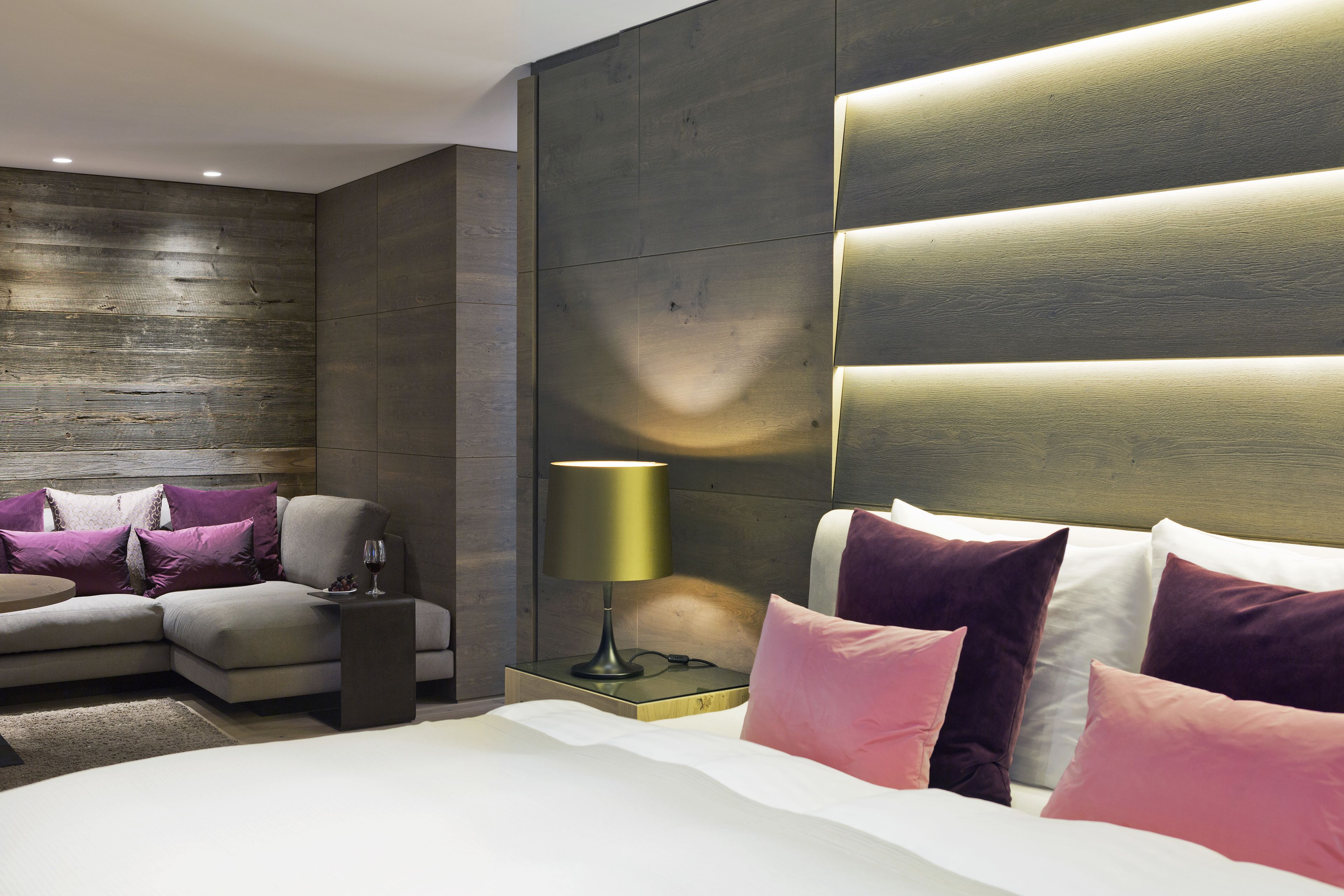 Een moderne slaapkamer met een bed, nachtkastje, lamp en een zithoek met een bank en kussens.
