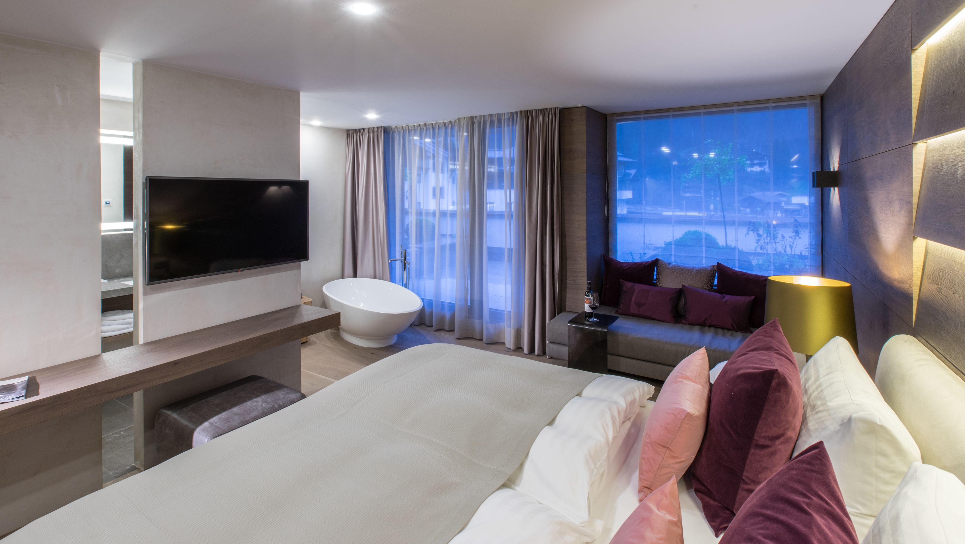 Habitación de hotel moderna con una cama grande, televisor, bañera y vistas a la ciudad.