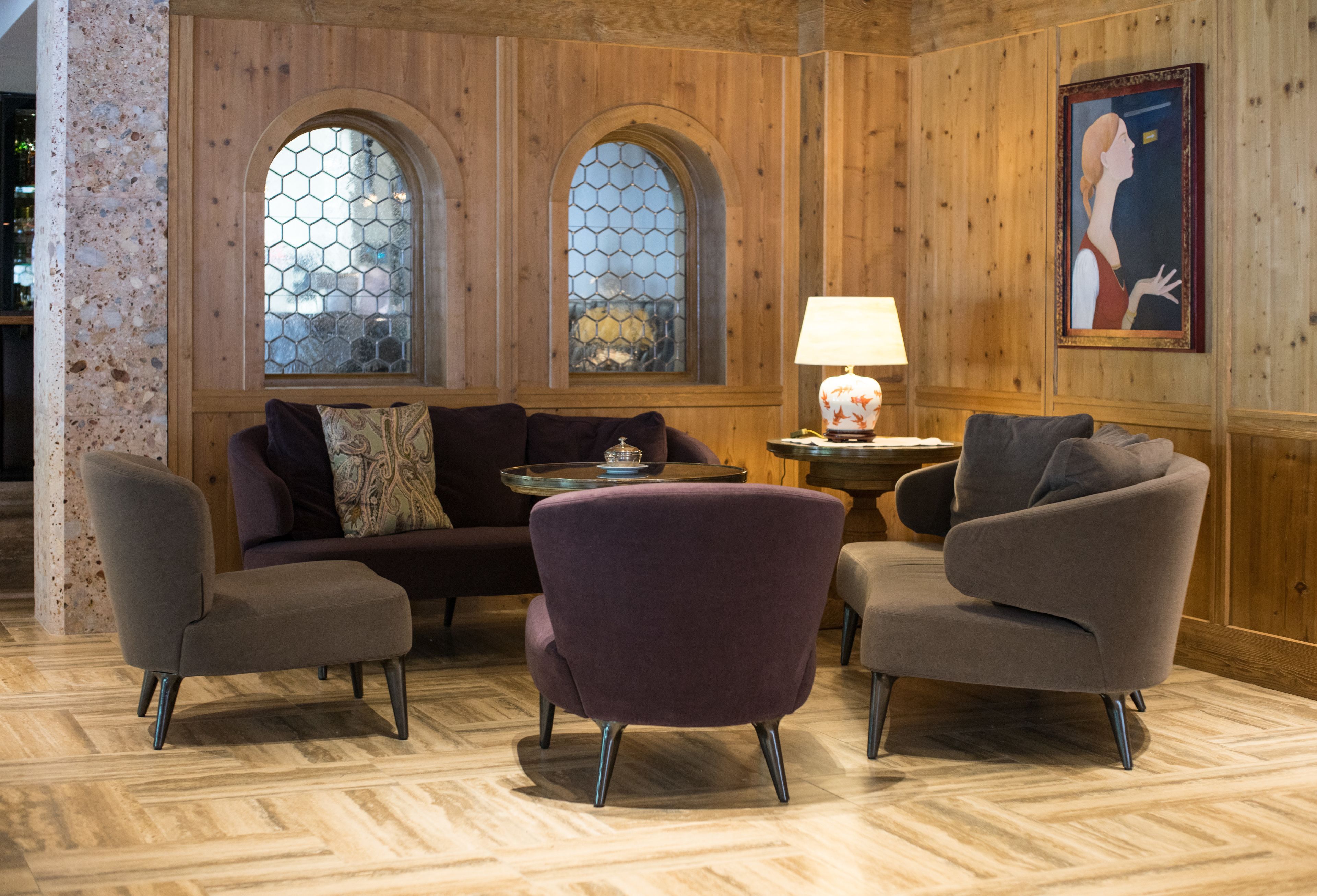 Une pièce avec un mur lambrissé en bois, un canapé, deux fauteuils, une petite table avec une lampe et un tableau.