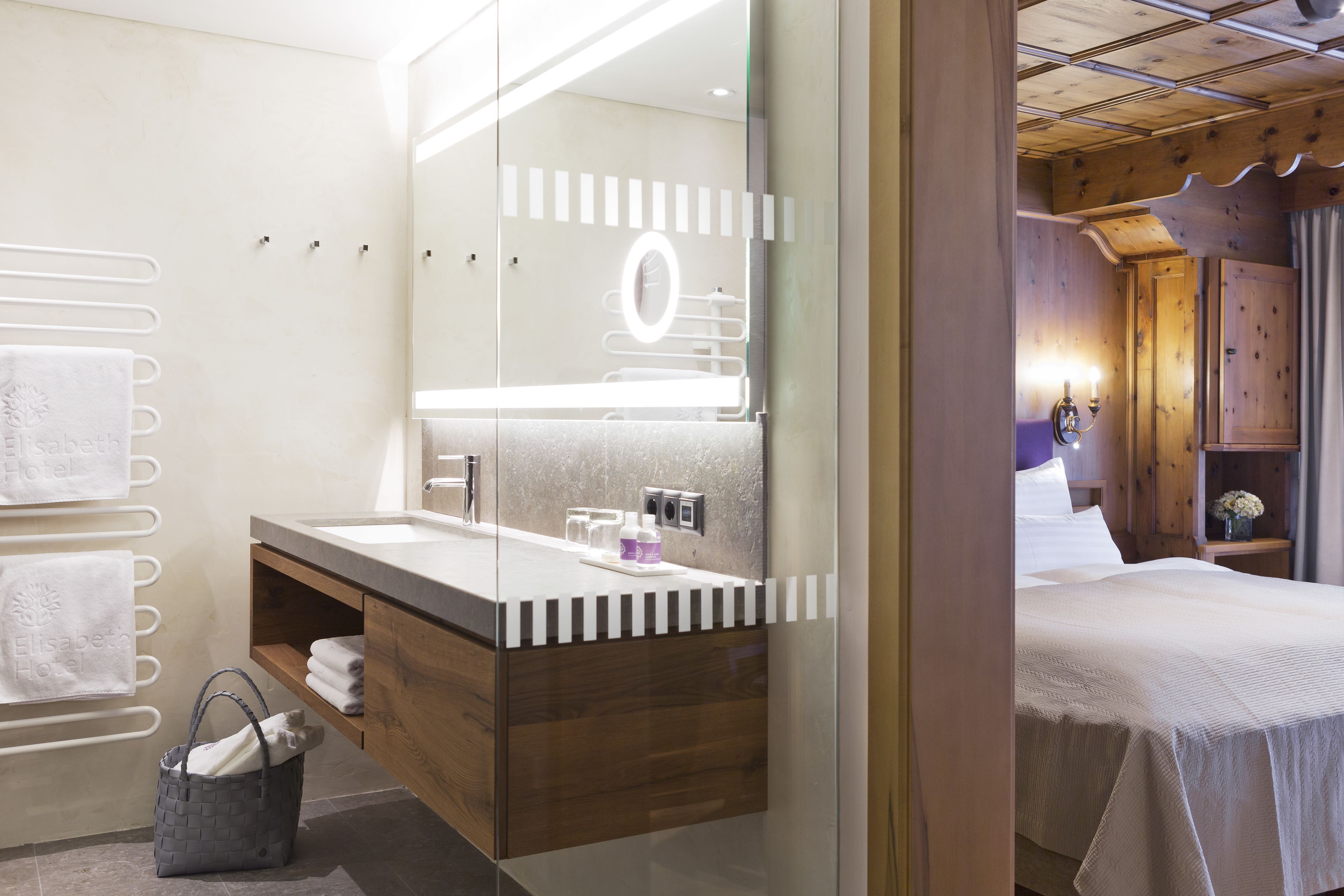 A modern bathroom with a large mirror, wooden vanity, and a bed with a white bedspread.