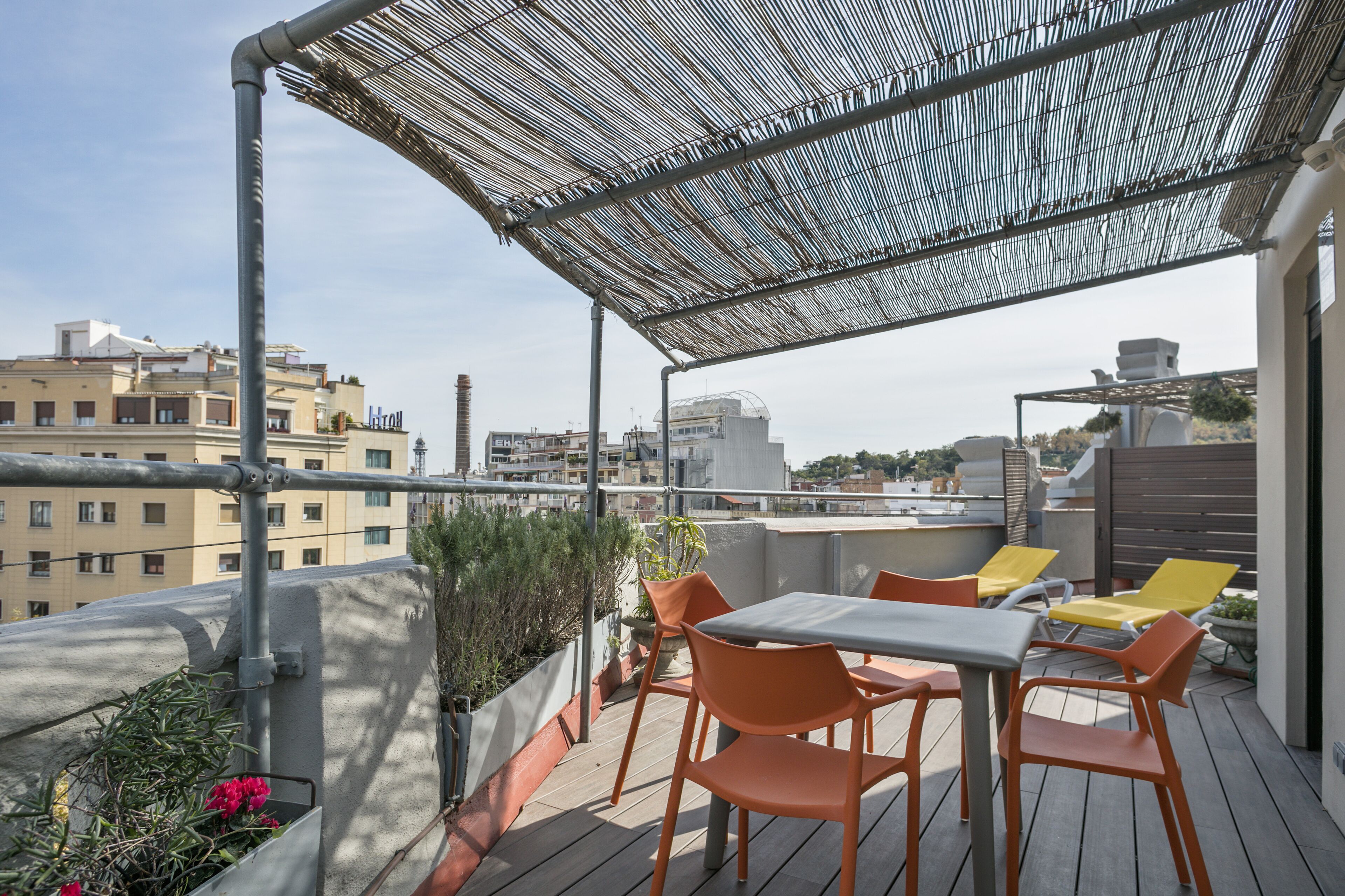 Una terraza en la azotea con mesa y sillas, una pérgola y vistas de la ciudad.