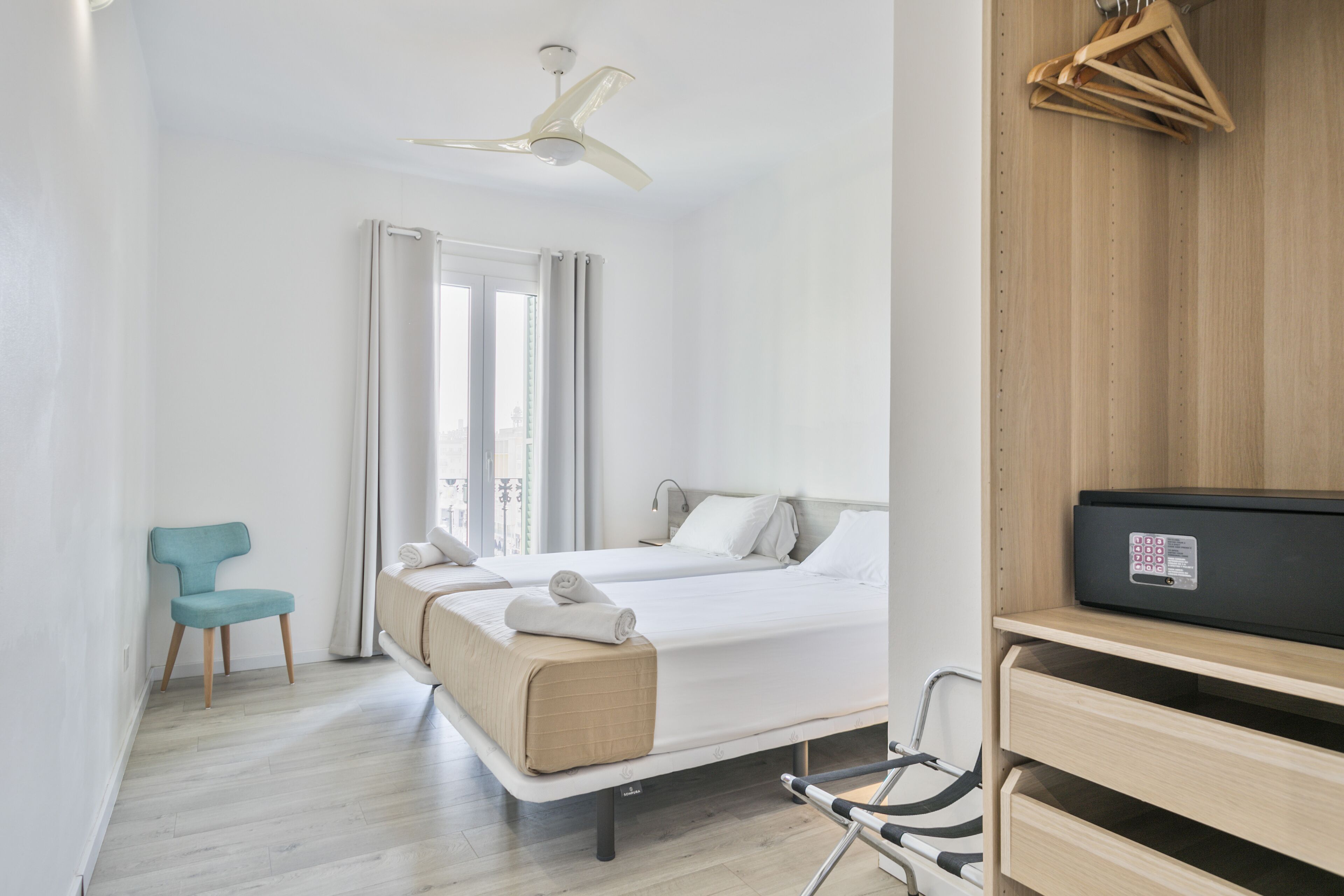 A hotel room with two beds, a ceiling fan, a wooden wardrobe, and a chair.