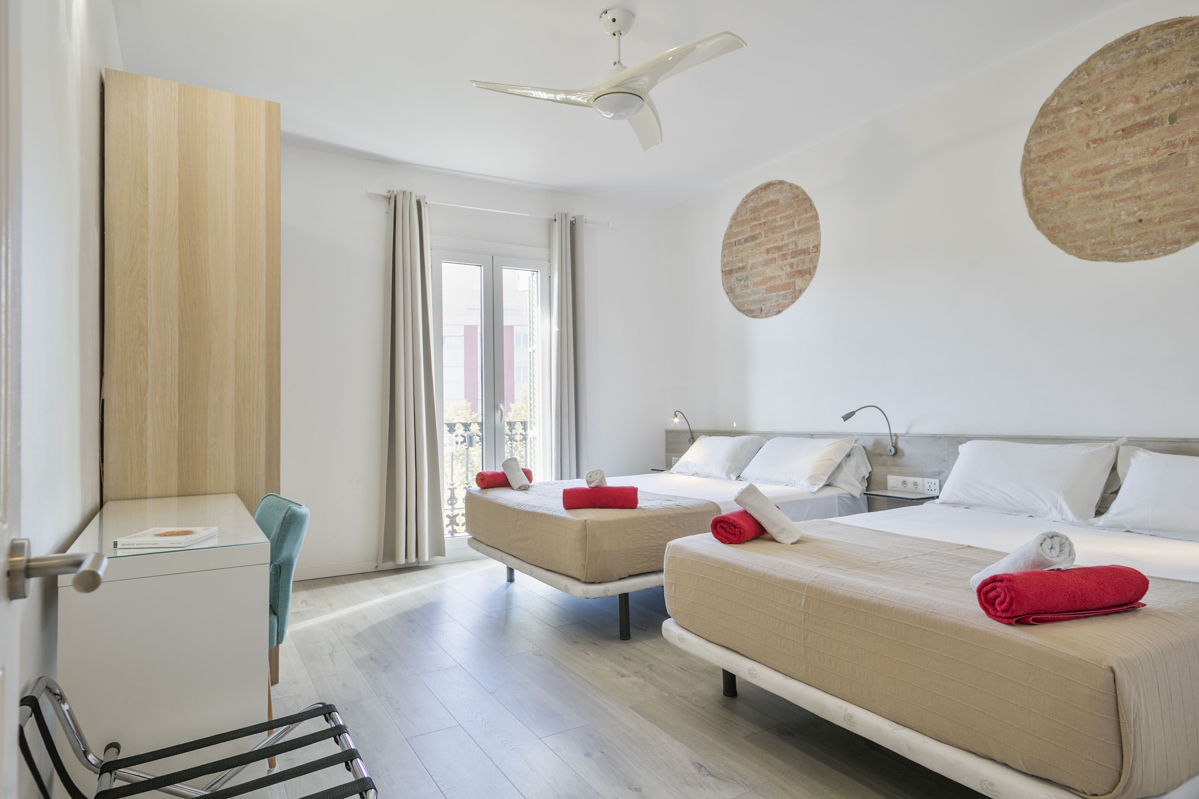 Habitación de hotel con dos camas, un escritorio, una silla, un ventilador de techo y una ventana con cortinas.