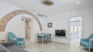 Uma sala de estar moderna com um arco de pedra, um espaço de jantar com cadeiras cor turquesa, um sofá cinza e uma TV de tela plana na parede.