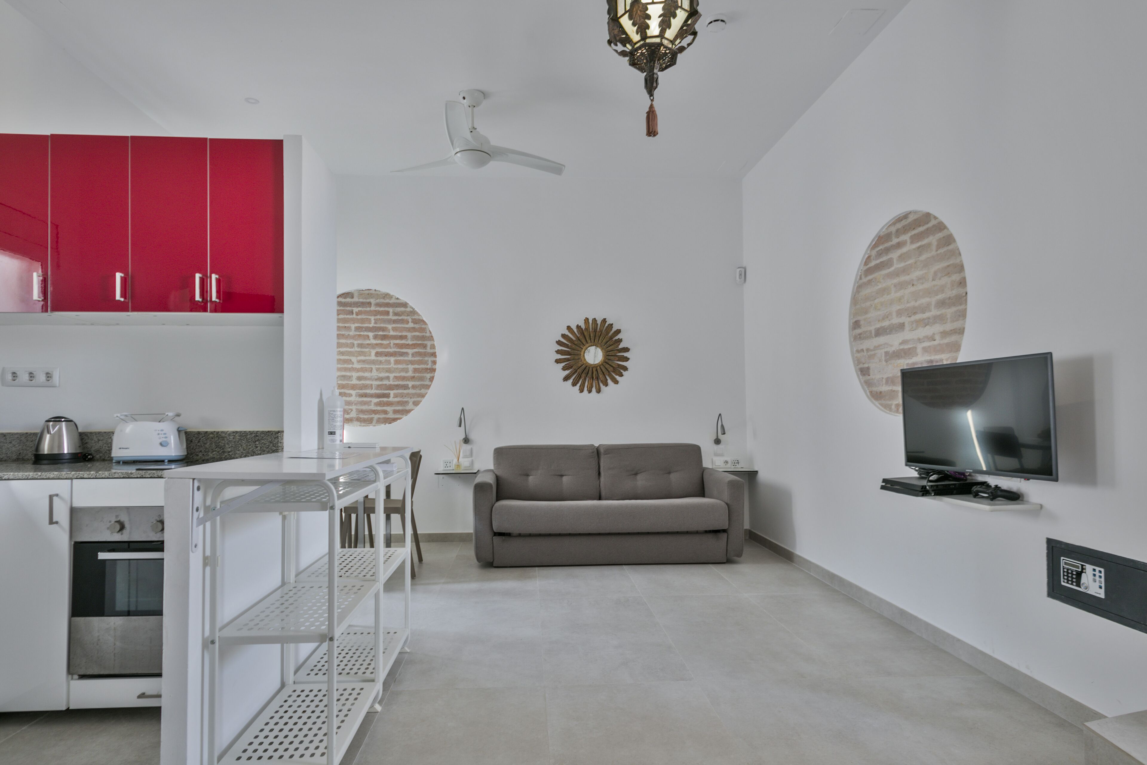 A modern kitchen with white cabinets, a red accent wall, a built-in oven, and a white ceiling fan.