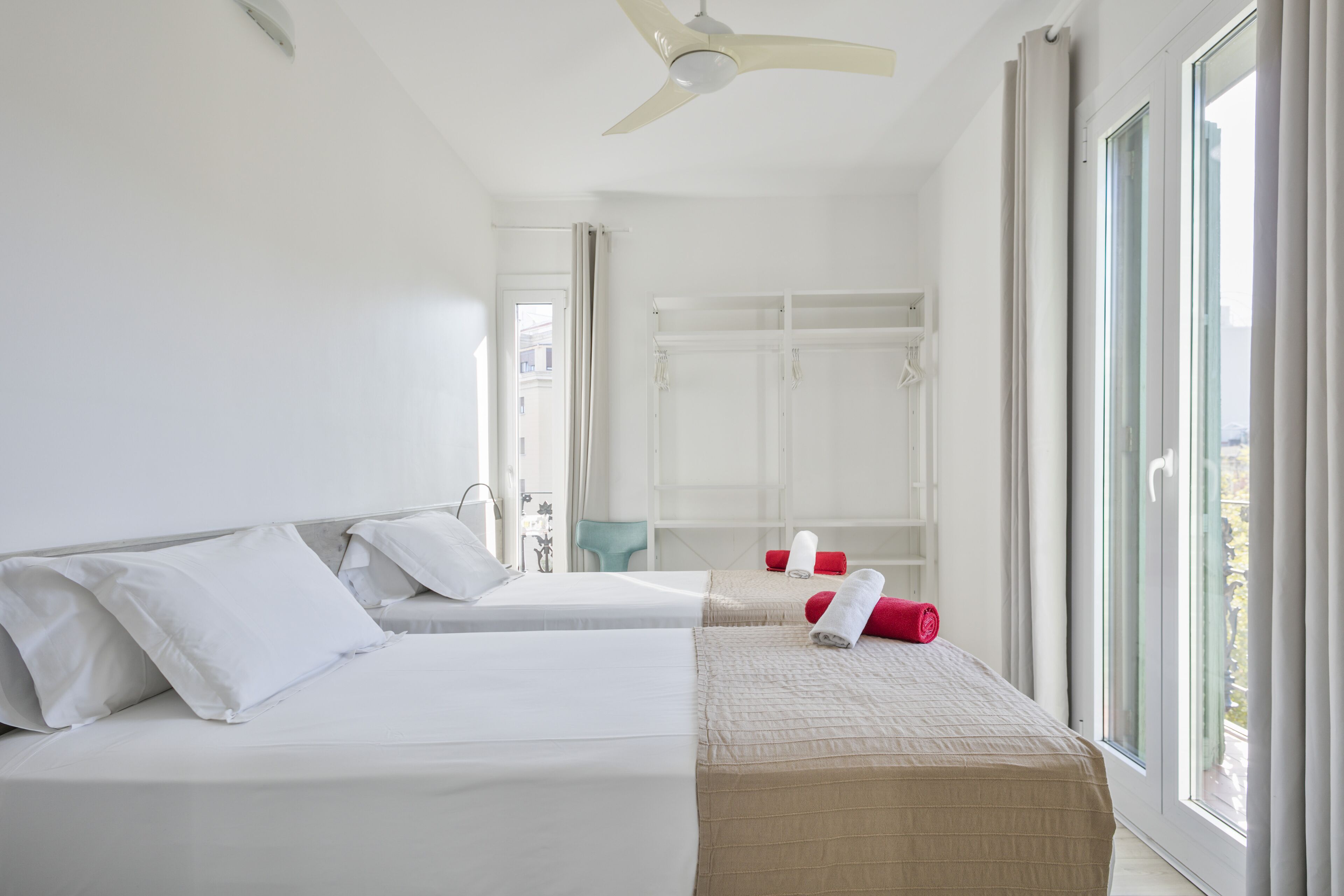 Habitación de hotel con dos camas, ventilador de techo, ventana con cortinas y vista al exterior.