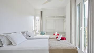 Habitación de hotel con dos camas, ventilador de techo, ventana con cortinas y vista al exterior.