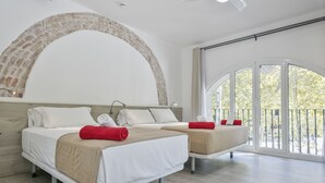 Quarto de hotel moderno com duas camas, uma grande parede de tijolos em arco e uma varanda com vista.