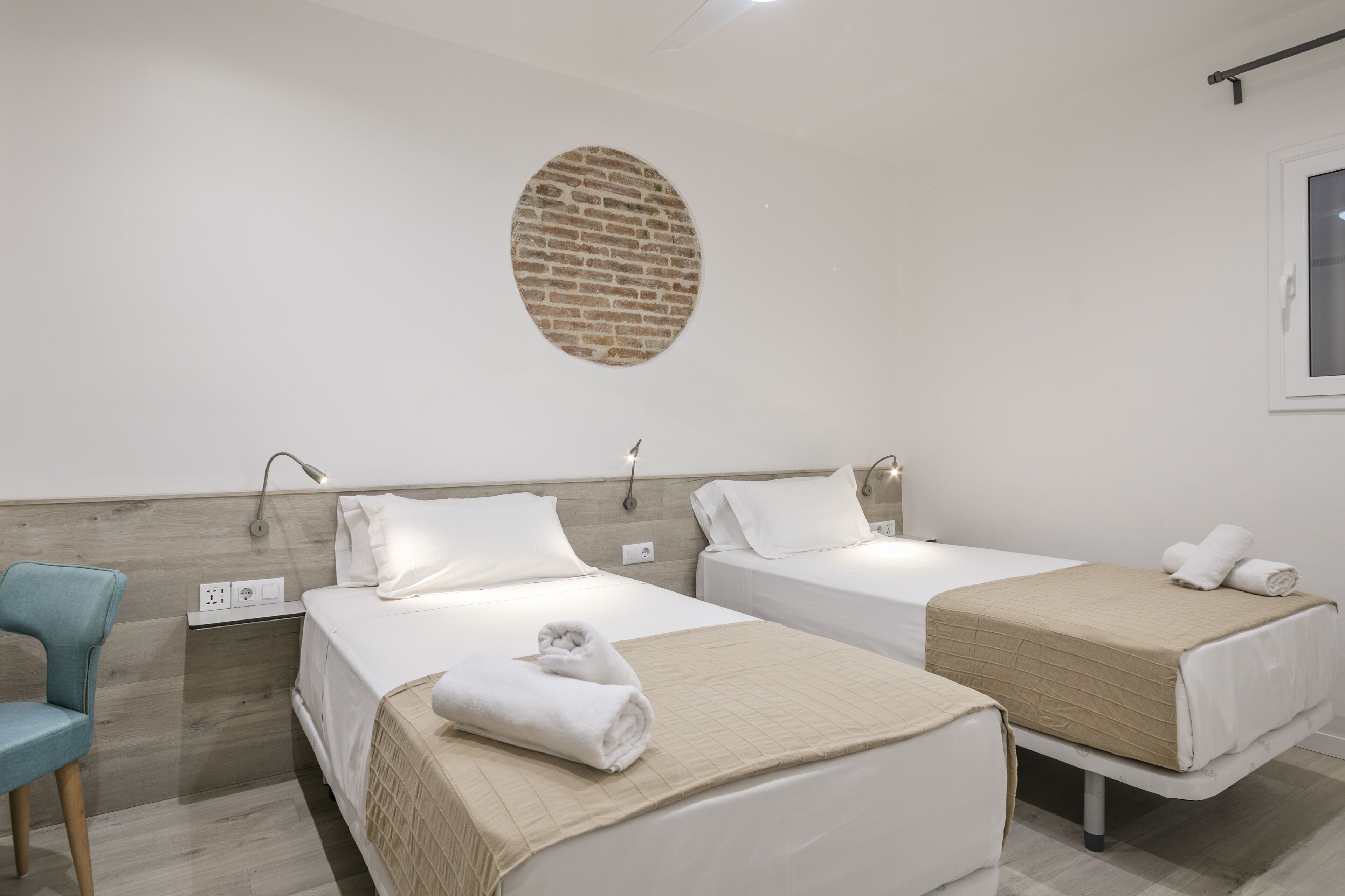 A hotel room with two beds, a round brick wall feature, and a window.